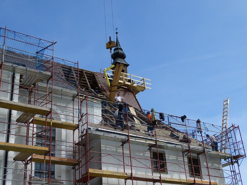 Kran transportiert Planken zu den Arbeitern auf dem Dach